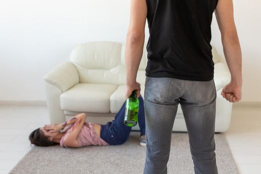 Victim, domestic violence, abuse and alcoholic concept - drunk man with bottle near his wife lying on the floor.