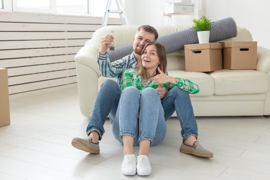 Young positive couple holding keys to a new apartment while standing in their living room. Housewarming and family mortgage concept