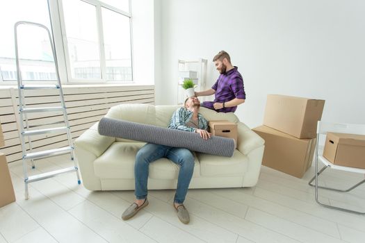 Two student male friends holding their things in their hands sitting in the living room of a new apartment. Housewarming concept.