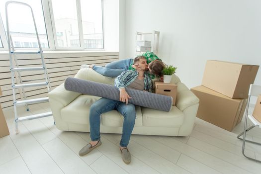 Moving, relocation and new home concept - young couple having fun on the couch surrounded with boxes.