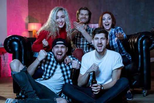 Group of friends having fun at home,watching game and enjoying together. Winners Friends are fans of sports games as football, basketball, hockey, baseball, love spending their free time at home together. They are screaming and gesturing for a victory