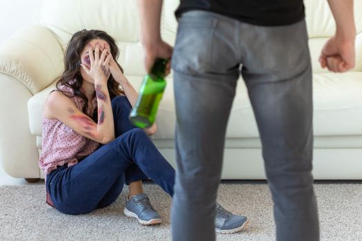 domestic violence, alcoholic and abuse concept - drunk man with bottle abusing his wife lying on the floor.