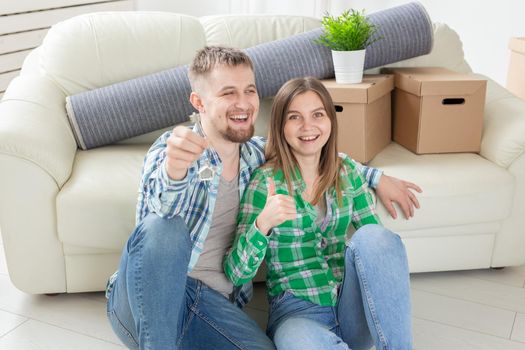 Young positive couple holding keys to a new apartment while standing in their living room. Housewarming and family mortgage concept