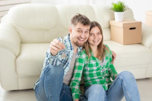 Young positive couple holding keys to a new apartment while standing in their living room. Housewarming and family mortgage concept