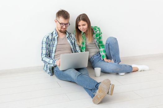 Charming young positive couple in casual clothes looking for an interior designer for their new apartment using a laptop and high-speed Internet. Apartment design concept