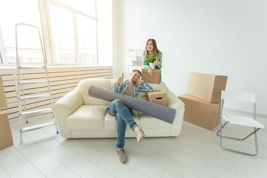 Satisfied cheerful young couple strong man and pretty woman holding their things in their hands sitting in the living room of a new apartment. Housewarming concept