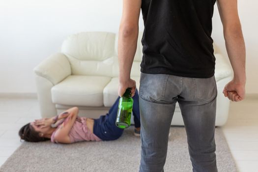 Victim, domestic violence, abuse and alcoholic concept - drunk man with bottle near his wife lying on the floor.