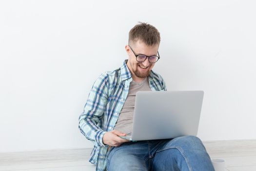 Positive young man in casual clothes and glasses surfing the Internet using Wi-Fi and a laptop in search of rental housing. Housewarming and apartment search concept