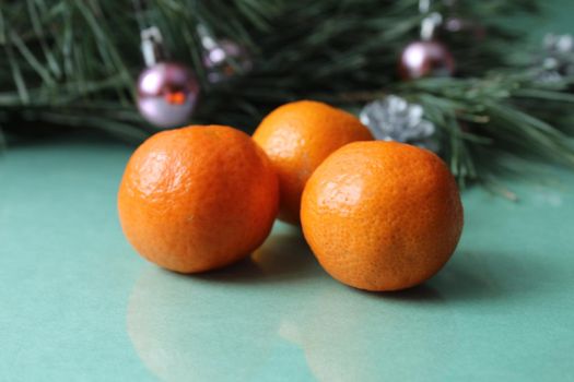 two three citrus tangerines in the peel of unpeeled lie next to a branch of a Spruce Tree tree on a green background. Christmas New Year's Eve atmosphere.