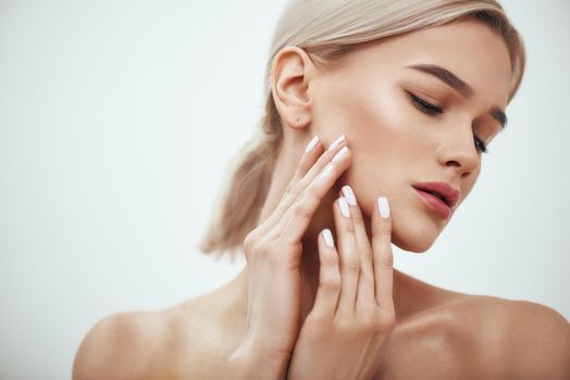 Perfect skin. Portrait of gorgeous blonde woman touching her soft glowing skin while standing against grey background. Skin care. Cosmetics concept