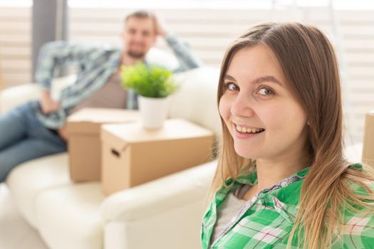 Positive smiling young girl sitting against her laughing blurred husband in a new living room while moving to a new home. The concept of joy from the possibility of finding new housing