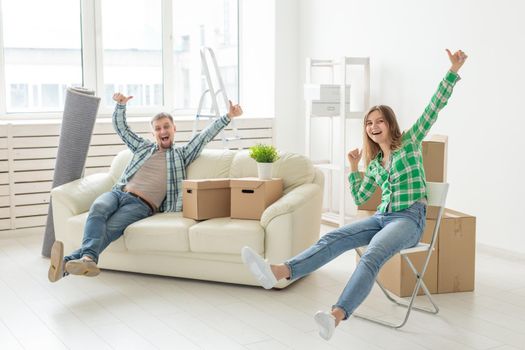 Positive crazy cheerful couple rejoices in moving their new apartment sitting in the living room with their belongings. Concept of housewarming and mortgages for a young family