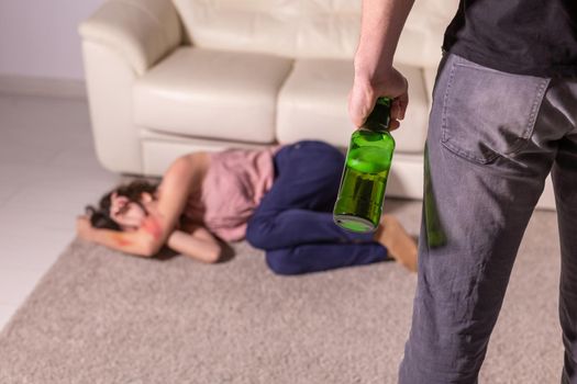 Alcoholism, abuse and domestic violence - Woman lying on the floor, afraid of men with bottle.