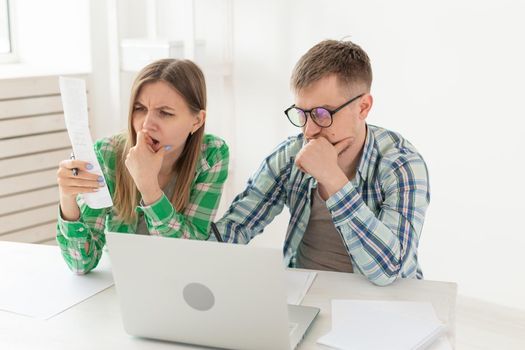 Surprised married couple. Husband and wife are considering bills for paying an apartment and are shocked at the amount received by writing down the results in their home accounting in a laptop