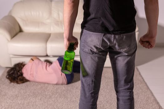 domestic violence, alcoholic and abuse concept - drunk man with bottle abusing his wife lying on the floor.