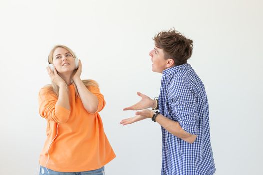 Young upset man begs his woman to listen to him but she listens to music with headphones posing on a white background. Misunderstanding and unwillingness to engage in dialogue