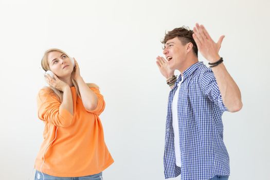 Young upset man begs his woman to listen to him but she listens to music with headphones posing on a white background. Misunderstanding and unwillingness to engage in dialogue