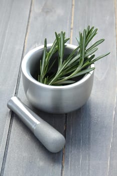 Metal mortar and pestle with rosemary on wooden background