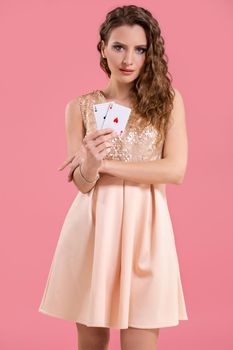 Young beautiful woman playing in casino. Woman in light dress holding the winning combination of poker cards on pink background. Two aces