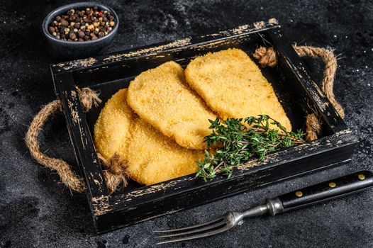 Raw chicken cordon bleu meat cutlets in a wooden tray with herbs. Black background. Top view.