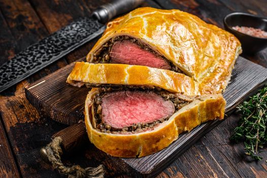 Homemade Beef Wellington puff pie with tenderloin meat on a cutting board. Dark wooden background. Top view.