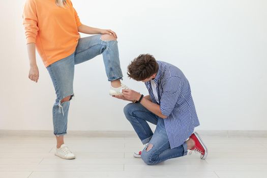 Young man is kneeling and reverently tying shoelaces to his domineering unidentified woman posing on a white background. Concept of dominant relationships