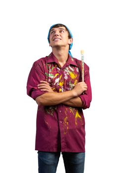 Smiling young painter artist holding paintbrush. Portrait of happy decorator looking upwards isolated on white background. Artistic occupation and creative profession. Art school student posing.