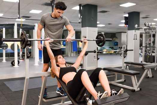 Personal trainer helping a young woman lift weights while working out in a gym