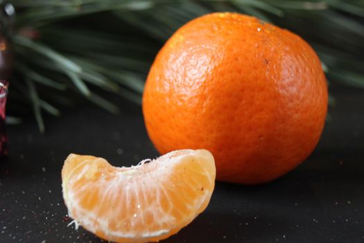 mandarin whole in the peel and a slice of fruit lie side by side on a black background next to a branch of spruce and a silver cone. New Year and Christmas. holiday attribute.