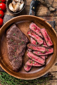 Grilled sliced top blade or denver beef meat steak in a wooden plate with herbs. wooden background. Top view.
