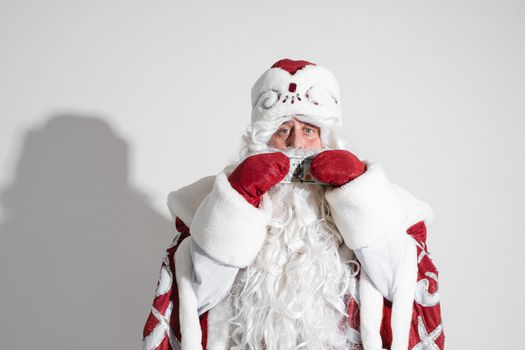 Smiling generous Santa Claus with long white beard in fancy costume holding banknote in hands wearing red mittens. Cutout on white background.