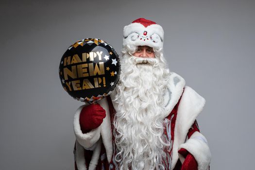 father frost with long beard holds a black baloon and looks to the camera, picture isolated on grey background