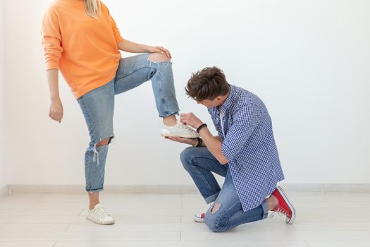 Young man is kneeling and reverently tying shoelaces to his domineering unidentified woman posing on a white background. Concept of dominant relationships