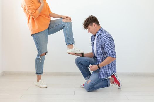 Young man is kneeling and reverently tying shoelaces to his domineering unidentified woman posing on a white background. Concept of dominant relationships