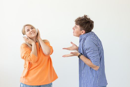 Young upset man begs his woman to listen to him but she listens to music with headphones posing on a white background. Misunderstanding and unwillingness to engage in dialogue