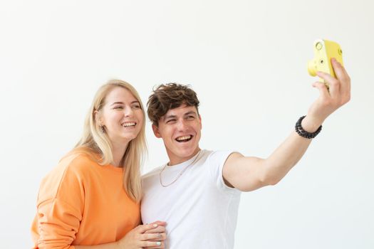 Funny young couple in love cute man and charming woman making selfie on vintage yellow film camera posing on a white background. Concept lovers of photography and hobbies. Advertising space