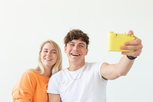 Funny young couple in love cute man and charming woman making selfie on vintage yellow film camera posing on a white background. Concept lovers of photography and hobbies. Advertising space