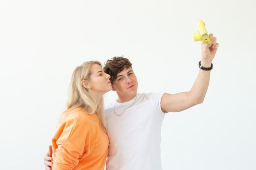 Funny young couple in love cute man and charming woman making selfie on vintage yellow film camera posing on a white background. Concept lovers of photography and hobbies. Advertising space