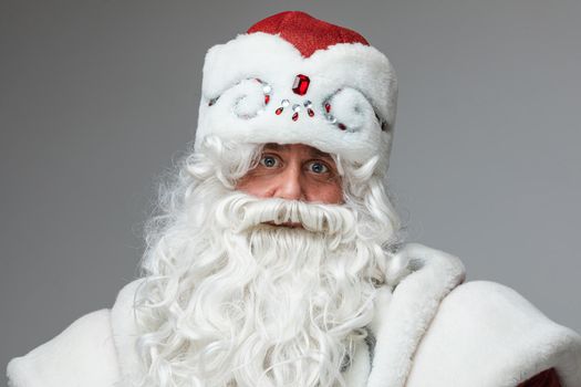 Stock photo of smiling happy Santa in traditional hat with rhinestones and long white beard looking at camera. Cutout on red background. Happiness concept.