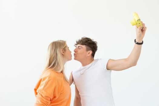 Funny young couple in love cute man and charming woman making selfie on vintage yellow film camera posing on a white background. Concept lovers of photography and hobbies. Advertising space