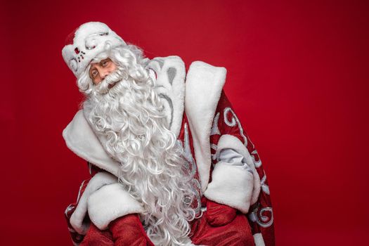 Portrait of a white-bearded Santa with long white beard in traditional fancy costume looking at camera leaning to the right.