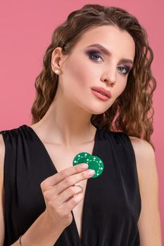 Portrait of a beautiful young woman with poker chips on pink background. Studio shot