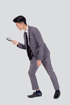 Young asian business man in suit look at magnifying glass for search isolated on white background, businessman expression and find quality, full length, inspector and scrutiny, male expression.