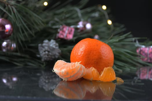 mandarin and slices of mandwrin lie near the Christmas tree with cones and lights. New Year's atmosphere.