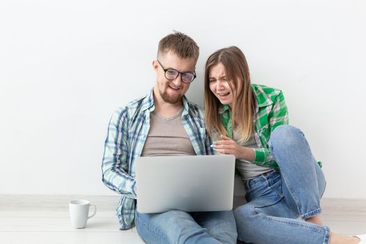 Smiling young couple makes online purchases of furniture in their new mortgage apartment. Online shopping concept with laptop and gadgets. Copyspace