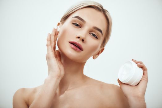 Best moisturizer for your skin type. Portrait of gorgeous young woman spreading cream on her face. Studio shot. Skin care. Beauty concept. Cosmetics concept