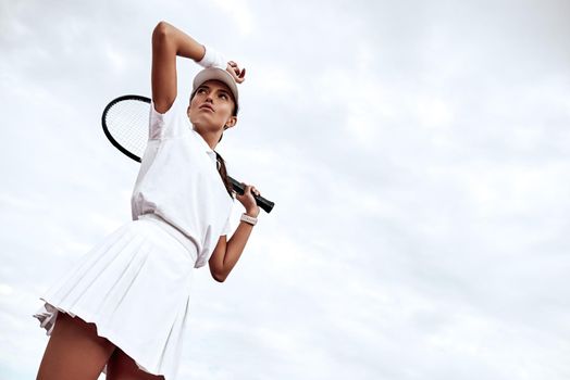 Beautiful girl in white polo and skirt is standing on the court with a racket in her hand looking away