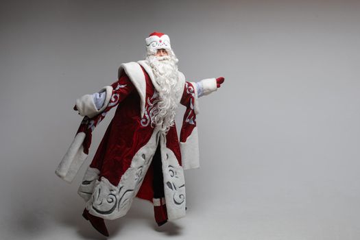 Full length of Father Frost in traditional costume jumping with arms outstretched and looking at camera. Isolated on grey background.