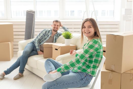 Positive smiling young girl sitting against her laughing blurred husband in a new living room while moving to a new home. The concept of joy from the possibility of finding new housing