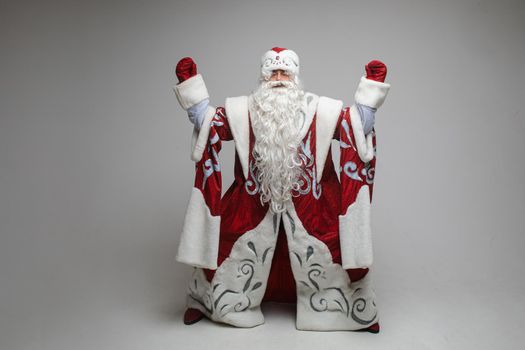 Stock photo of Father Frost in fancy costume making zen gestures with both hands standing with wide legs. Isolate on grey. Meditation, zen, patience concept.
